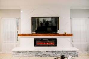 Un soggiorno moderno con una grande televisione a schermo piatto montata su una parete in marmo, un camino a incasso sottostante e uno scaffale in legno sopra.