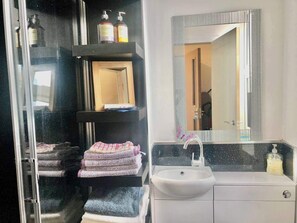 Bathroom features a sink, shower, and shelf with soap.
