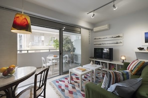 Un salon moderne comprenant un coin repas, un canapé, un téléviseur et un balcon aménagé avec du mobilier d’extérieur.