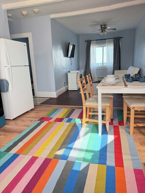 A modern kitchen with a white refrigerator, a dining table with chairs, a colorful striped rug, and a ceiling fan. - Charming 2-bedroom building in delightful Hull with ocean view (Hull)