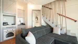 A modern kitchen with built-in appliances, a grey sectional sofa with white cushions, and a staircase with a rope railing.