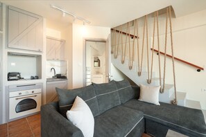 A modern kitchen with built-in appliances, a grey sectional sofa with white cushions, and a staircase with a rope railing. - Apartment 'Nest Luxury' with Sea View, Wi-Fi and Air Conditioning (Nikiana)