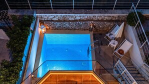 An outdoor swimming pool with a stone wall, a tiled deck, and a staircase leading to a covered area.