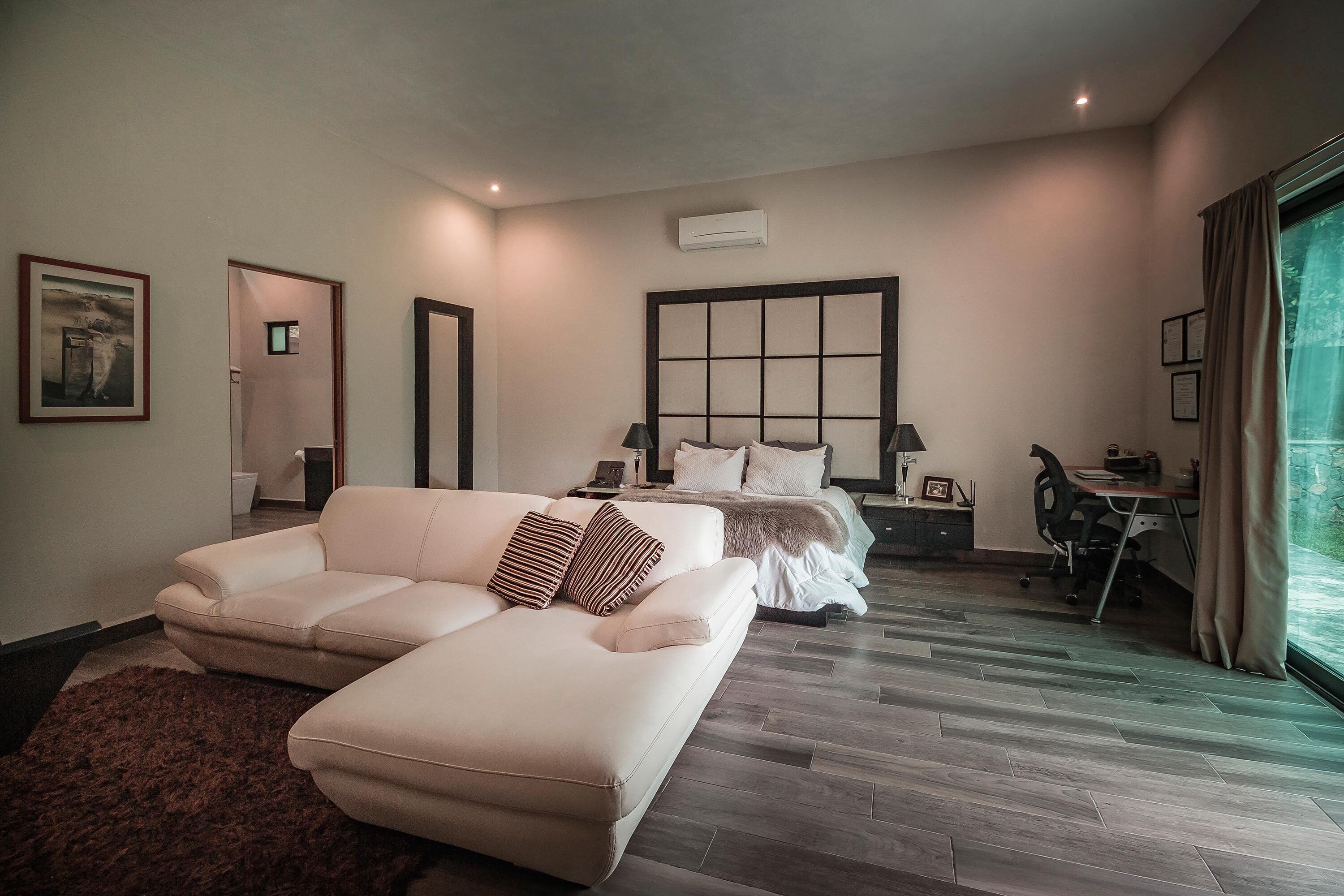 A modern hotel room with a large bed, a sofa, a desk, and a view of the outdoors.