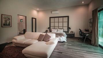 A modern hotel room with a large bed, a sofa, a desk, and a view of the outdoors.