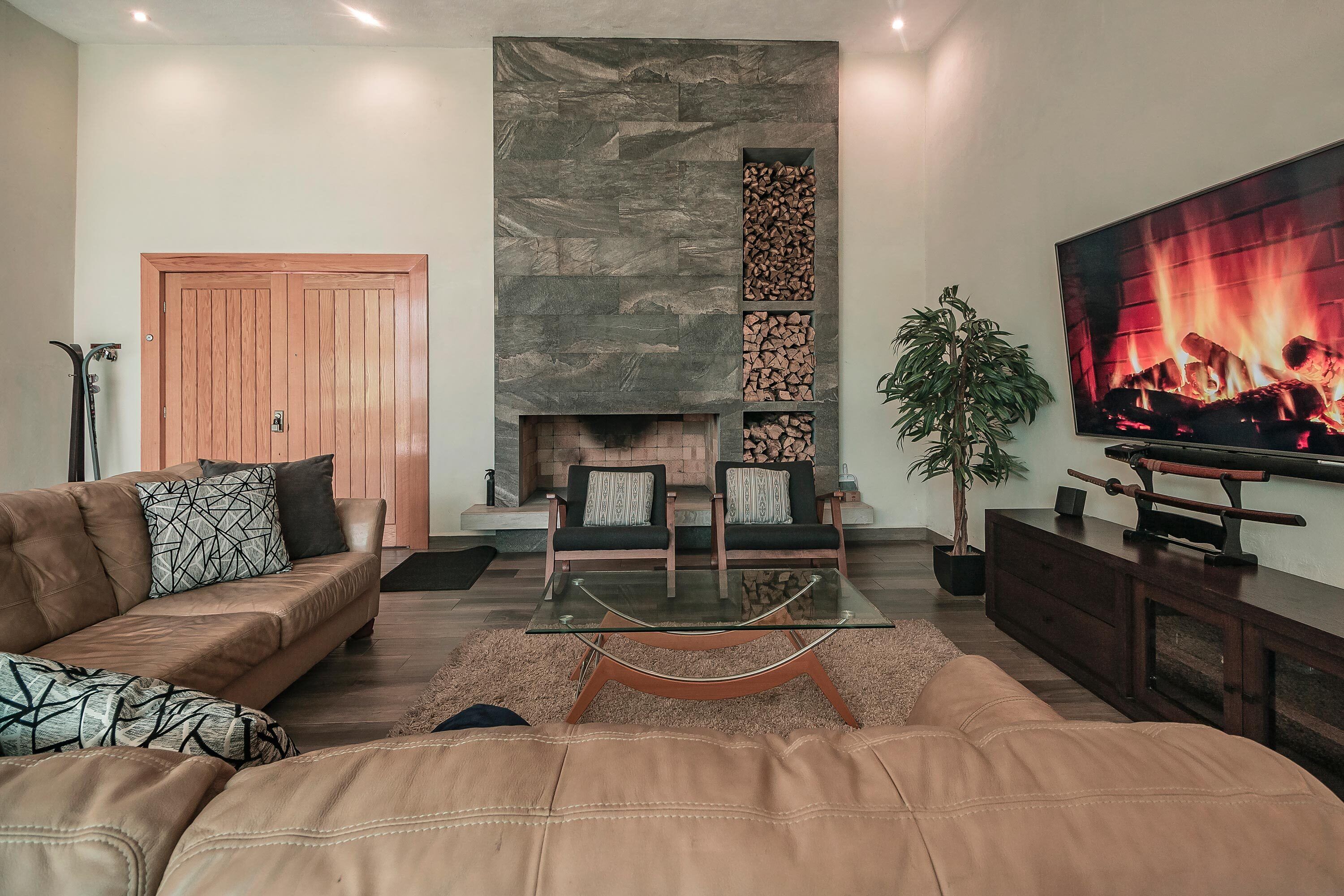 A living room with a stone fireplace, leather sofas, a glass coffee table, and a TV displaying a fireplace.
