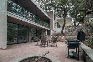Un pati exterior modern amb una paret de pedra, una barbacoa i una zona d'estar amb cadires i una taula.
