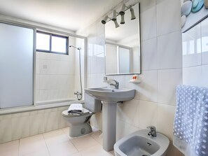 Et moderne badeværelse med badekar, toilet, vask, bidet og et stort spejl.