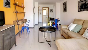 Una sala de estar con sofá, televisor, comedor con sillas y zona de cocina con refrigerador.