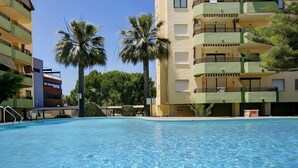 Una piscina con agua azul cristalina, rodeada de edificios de varios pisos con balcones y palmeras.