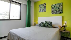 Habitación de hotel con una cama, un ventanal con cortinas, una pared verde y dos cuadros colgados.