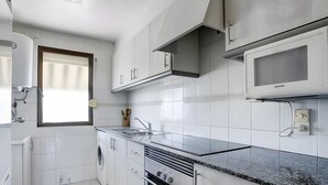 Una cocina moderna con armarios blancos, horno empotrado, microondas y una ventana con persianas.