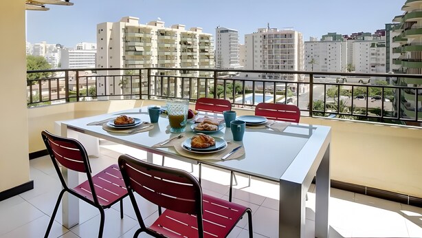 Un balcón con una mesa para dos, sillas y vistas de edificios circundantes.