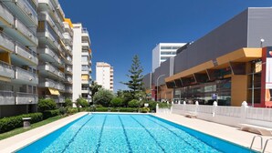 A swimming pool surrounded by multi-story buildings, a clear sky, and some greenery. - 'Terrazas Playa Gandia' Apartment with Sea View, Wi-Fi and Air Conditioning (Grau i Platja)