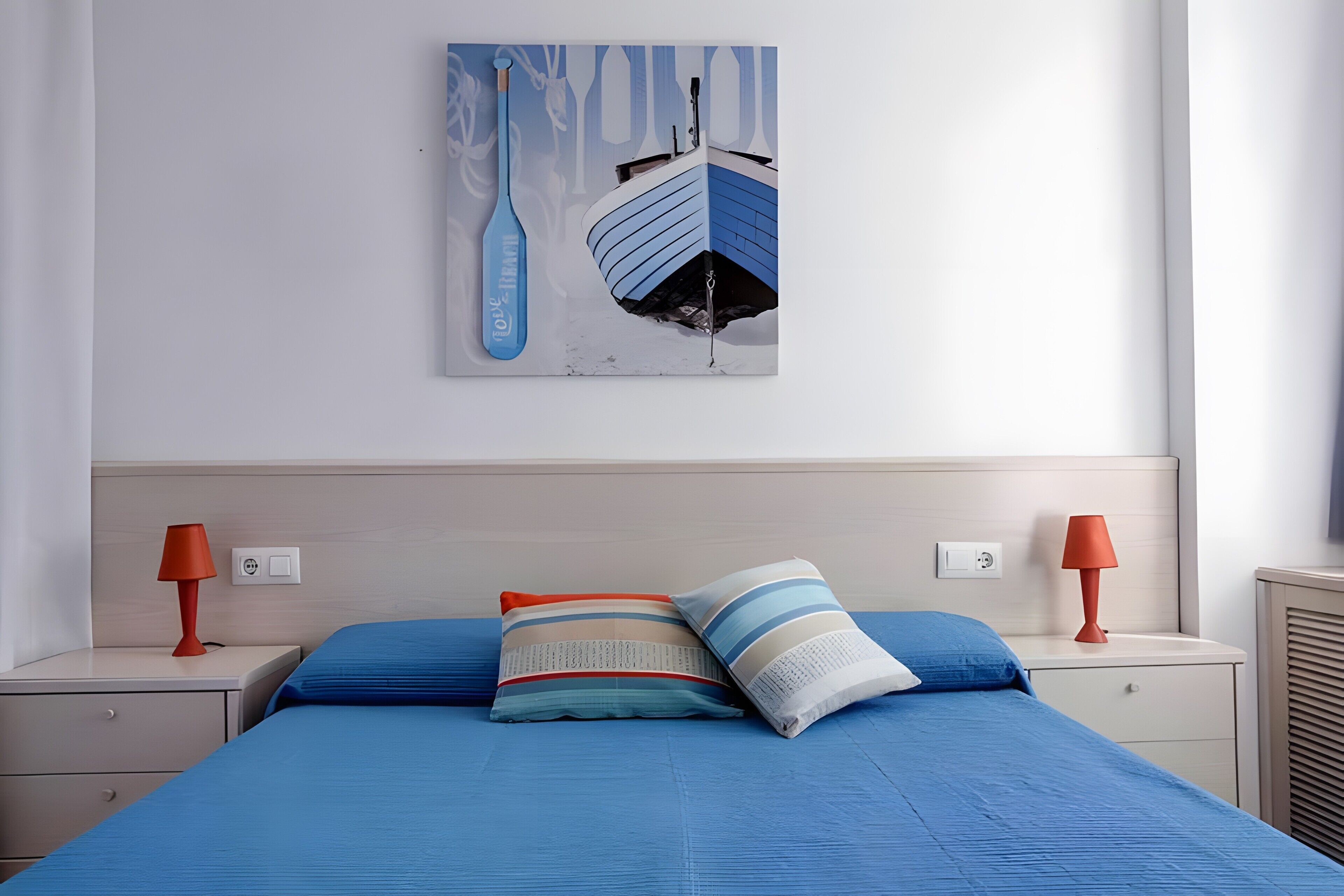 A bedroom with a bed, two nightstands, a lamp, a painting, and a radiator.