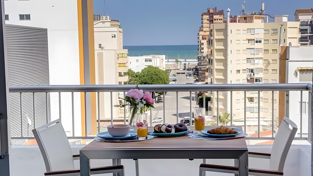 A balcony with a table set for breakfast, overlooking a cityscape and the sea. - 'Terrazas Playa Gandia' Apartment with Sea View, Wi-Fi and Air Conditioning (Grau i Platja)