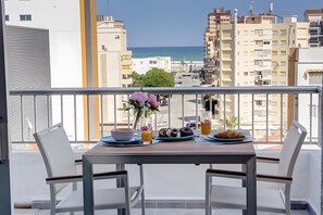 A balcony with a table set for breakfast, overlooking a cityscape and the sea.