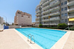 Ein Schwimmbecken mit Metallleitern, umgeben von einer gefliesten Terrasse, mit Wohngebäuden im Hintergrund.