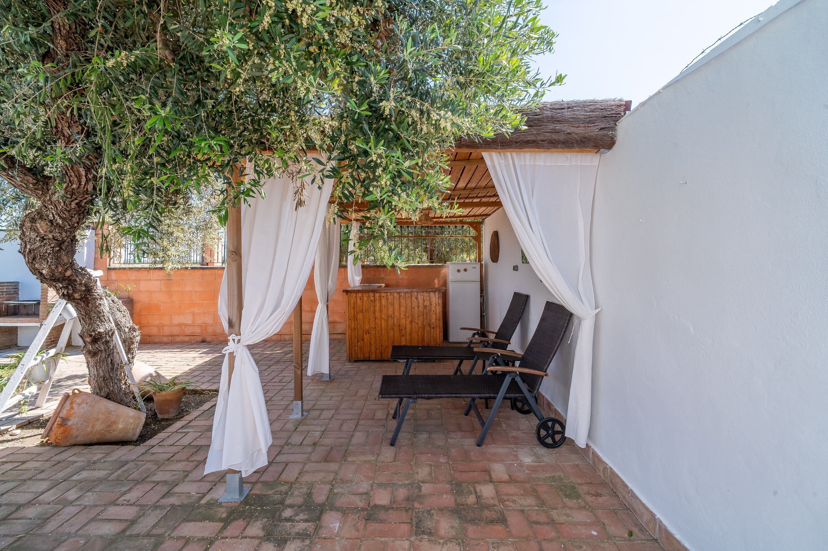 A patio with a wooden table, two lounge chairs, and a white wall.