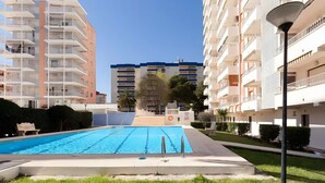 A modern apartment building with a swimming pool, balconies, and a clear sky.