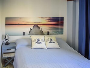 A bed with two pillows, a nightstand with a lamp, and a wall with a sunset painting.