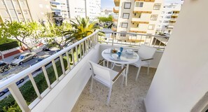 A balcony with a round table and chairs, a railing, and a view of the street and buildings.