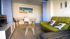 A compact living space with a green sofa, a small round table, and a TV on a white cabinet.