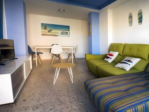 A compact living space with a green sofa, a small round table, and a TV on a white cabinet.