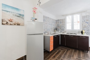 A kitchen with a white refrigerator, orange drawers, patterned backsplash, and a window with blinds.