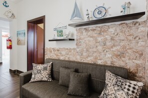 A reception area with a stone wall, a wooden door, a sofa with patterned cushions, and nautical decor.