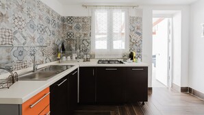 A kitchen with a sink, stove, and cabinets, a window with curtains, and a door leading to another room. - Apartment 'Maresol' with Private Terrace, Wi-Fi and Air Conditioning (Marsala)