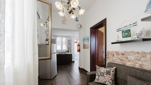 A hotel lobby with a wooden floor, a sofa with a patterned pillow, a chandelier, a kitchen area, and a stone wall. - Apartment 'Maresol' with Private Terrace, Wi-Fi and Air Conditioning (Marsala)