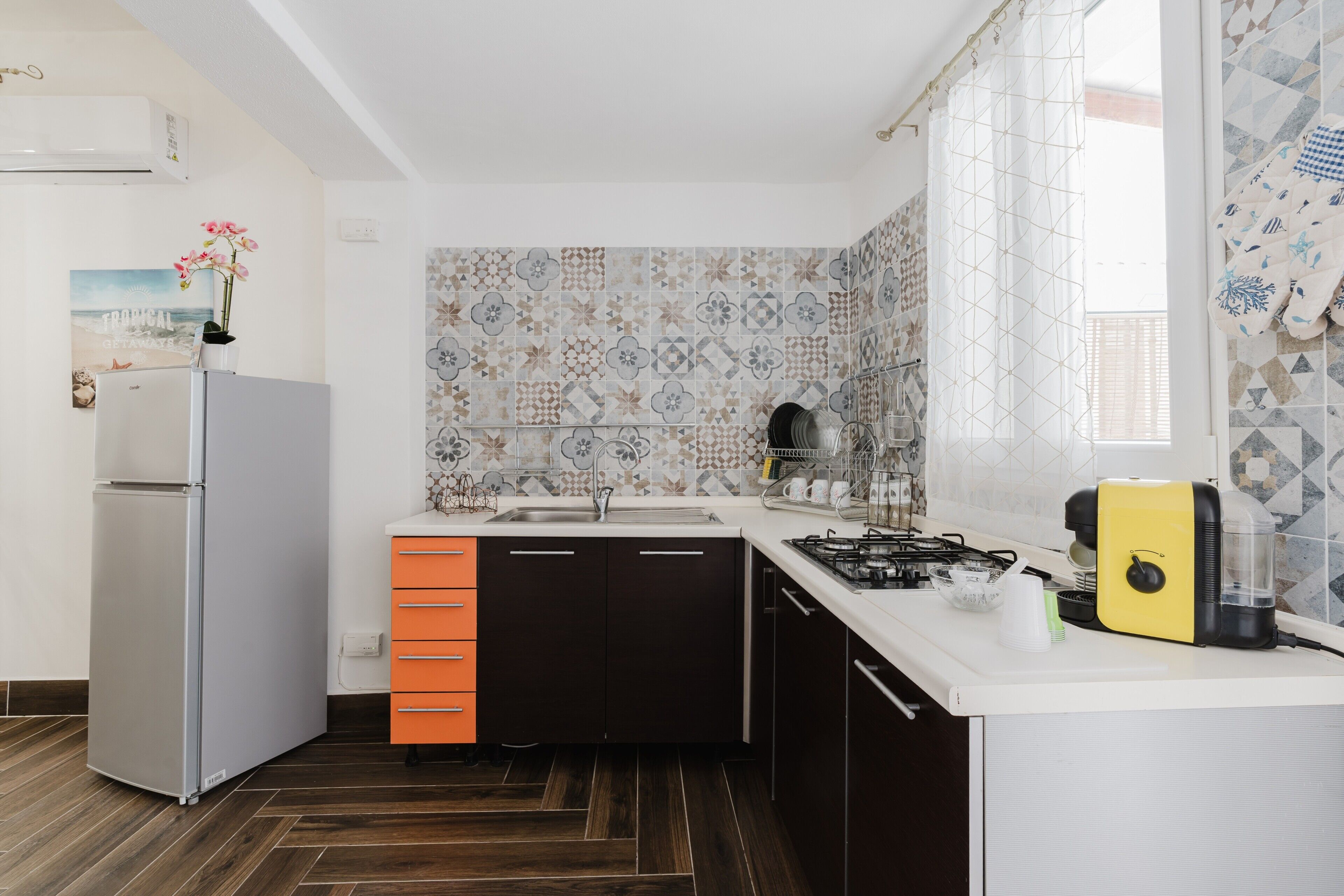 Cocina compacta con refrigerador, pileta y estufa, destacando baldosas estampadas y piso de madera.