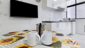 A modern kitchen with white cabinets, a coffee maker, and a flat-screen TV mounted on the wall.