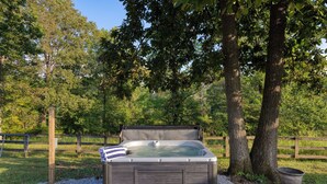 A hot tub in a natural setting with trees and a wooden fence. - Amber Cabin by Avantstay Cozy Mountain Retreat (New Market)