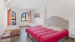Een slaapkamer met een groot bed, een kleiner bed, een raam en een nachtkastje.
