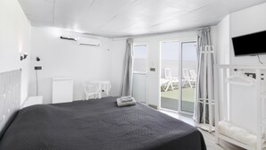Una habitación de hotel con cama, televisión, escritorio, silla y balcón con mobiliario exterior.