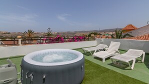 Una terraza en la azotea con un jacuzzi, sillas reclinables blancas y vistas del paisaje.