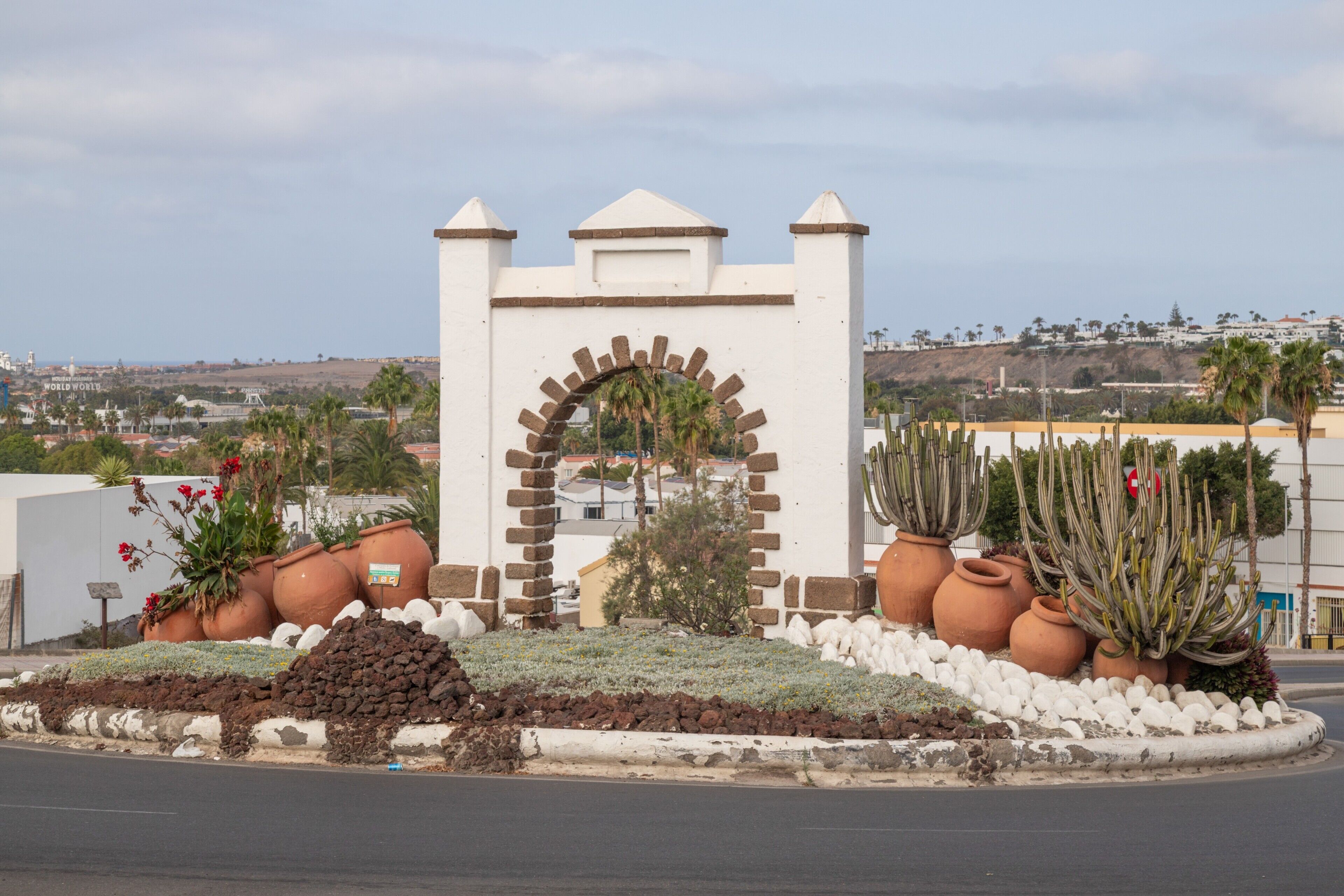 Un edificio bianco con un arco centrale, circondato da vasi in terracotta e cactus, con vista su un paesaggio collinare sullo sfondo.