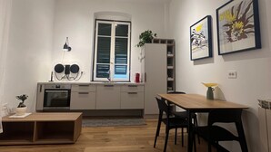 Un espacio habitable compacto con kitchenette, comedor y un amplio ventanal.