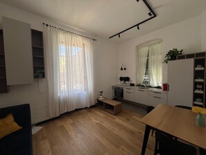 A compact kitchen with a built-in oven, a sink, and a small countertop. There is a dining area with a wooden table and chairs.