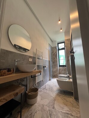 Un baño moderno con un espejo ovalado grande, un lavabo sobremesa, una bañera independiente y una ducha a pie.