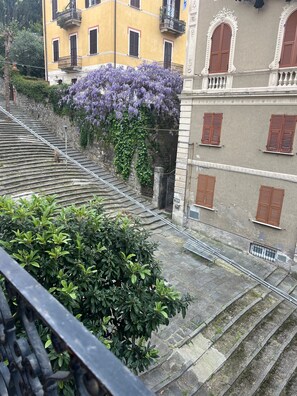 A staircase leading to a building with a yellow facade, red shutters, and a purple flowering vine.