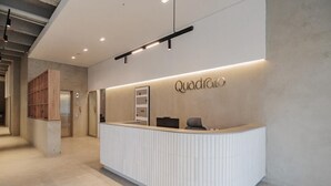 A modern reception area with a white reception desk, a wooden shelving unit, and a wall-mounted sign that reads "Quadras." - Charming 1-bedroom apartment with WiFi, AC in delightful Medellín (Medellín)