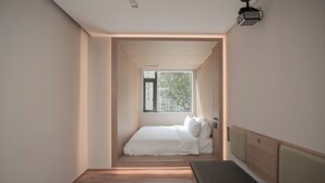 A narrow room with a bed, a bench, and a window providing natural light. - Shenzhen Enjoy Hotel (Huizhou)