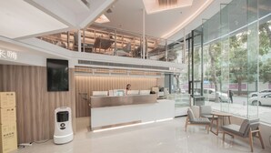 A modern hotel lobby with a reception desk, seating area, and a glass wall offering a view of the street. - Shenzhen Enjoy Hotel (Huizhou)