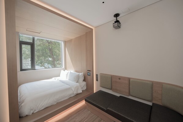 Une chambre moderne dotée d’un lit et d’un banc intégrés, de grandes fenêtres et d’un projecteur fixé au plafond.