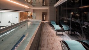 A modern indoor swimming pool with a long, narrow design, a seating area with cushioned chairs, and a visible reception desk. - Shenzhen Enjoy Hotel (Huizhou)