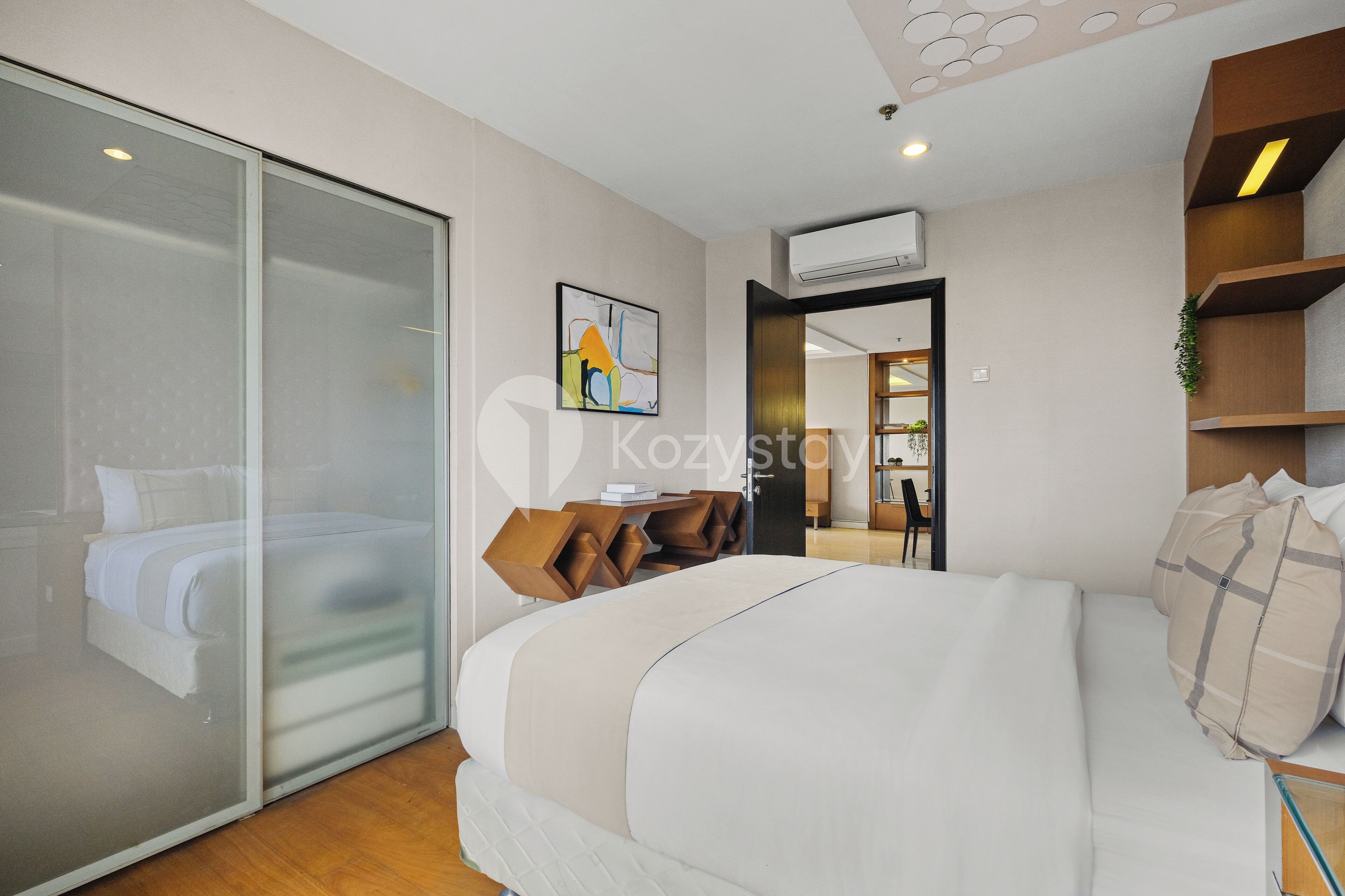 Une chambre d’hôtel moderne dotée d’un grand lit, d’une cloison en verre, d’une table de chevet en bois et d’un petit espace bureau.