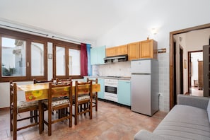 A compact kitchen with wooden cabinets, a dining table with chairs, and a refrigerator.